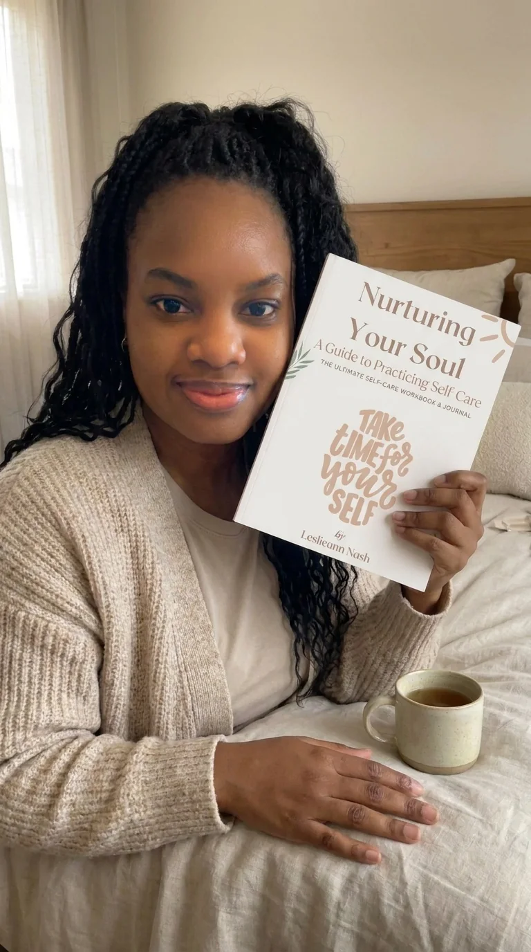 Leslieann sitting on a bed with a cup of tea, holding up her journal Nurturing Your Soul