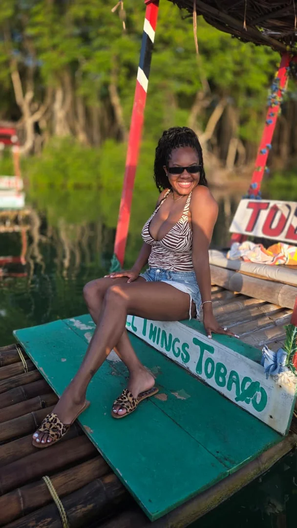 Leslieann seated on an All Things Tobago bamboo raft, with the operator's name painted on the deck