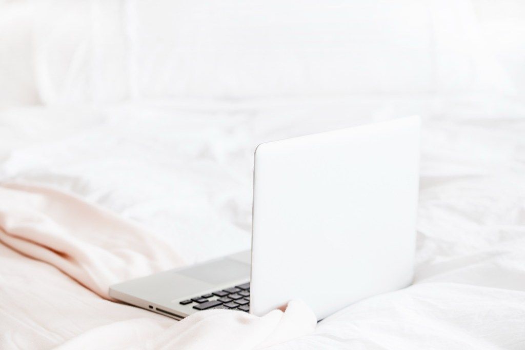 Woman using a laptop while sitting on white bedding
