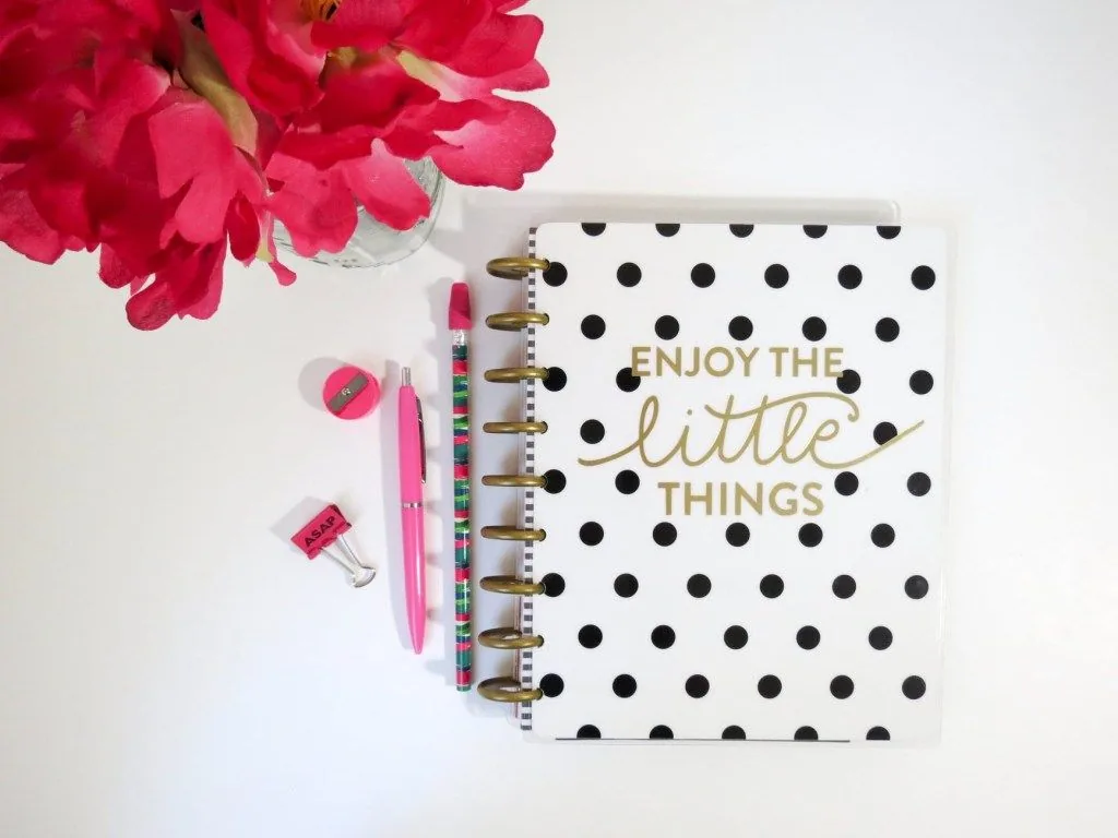 Notebook reading “Enjoy the little things” beside pink flowers