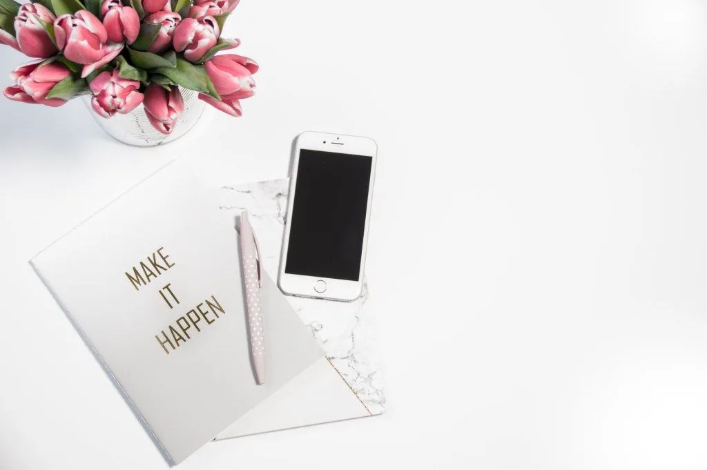 Phone and notebook reading “Make things happen” beside pink flowers