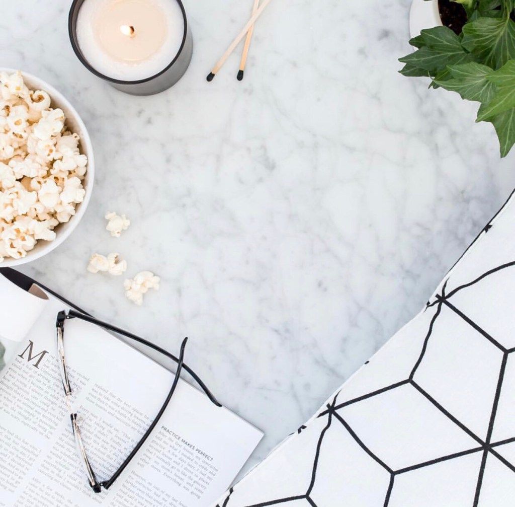 Candle, popcorn, glasses, and an open book on a marble table